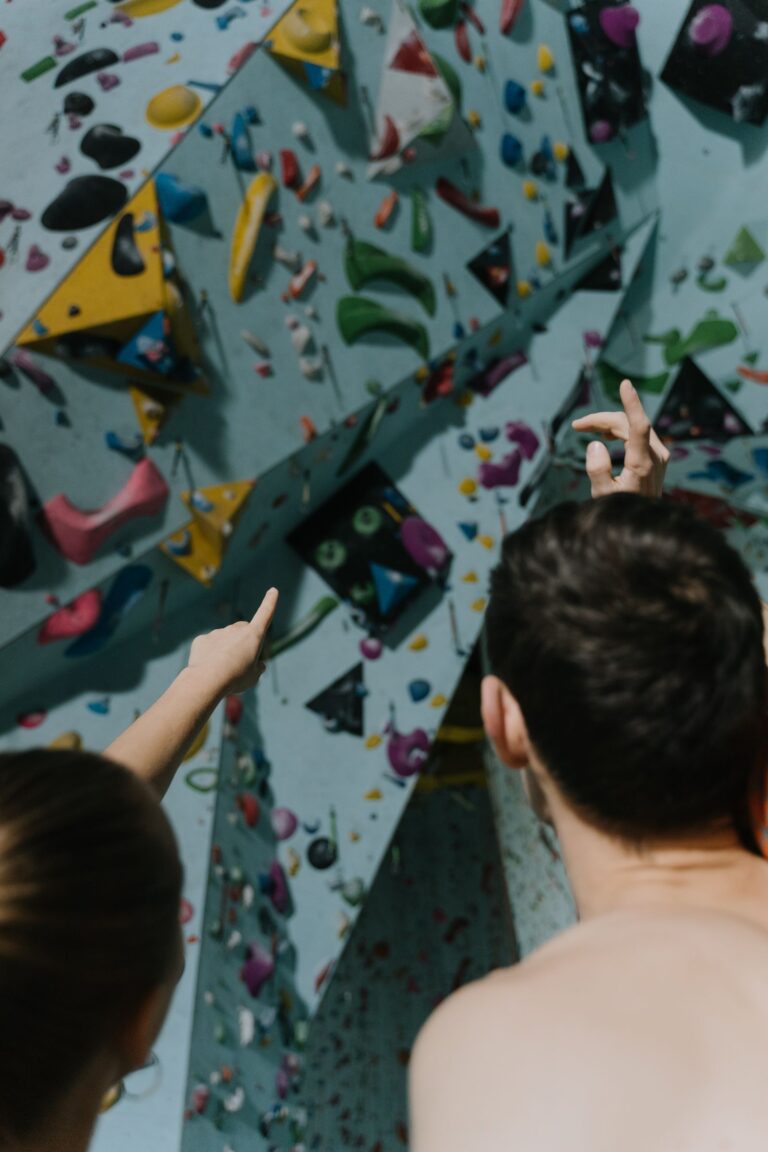 Zwei Menschen zeigen auf Griffe an einer bunten Kletterwand in einer Halle
